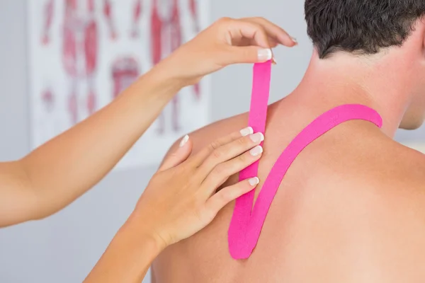 Физиотерапевт надевает розовую ленту кинезио на шею пациентам мужского пола — стоковое фото