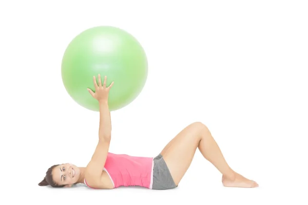 Smiling sporty brunette lying on floor holding exercise ball — Stock Photo, Image