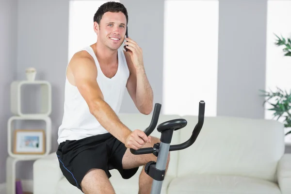 Fröhlicher sportlicher Mann, der auf dem Fahrrad turnt und telefoniert — Stockfoto