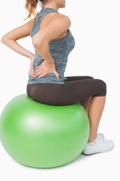 Mid section of young woman touching her back sitting on exercise ball — Stockfoto