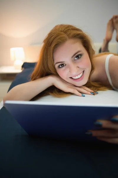 Ruiva atraente usando tablet digital deitado em sua cama sorrindo para a câmera — Fotografia de Stock