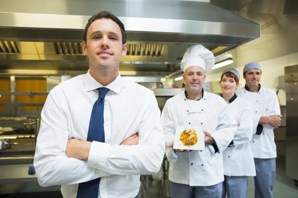 Jeune gérant de restaurant posant devant une équipe de chefs — Photo