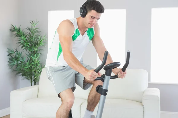 Esportivo homem bonito formação em bicicleta de exercício ouvir música — Fotografia de Stock