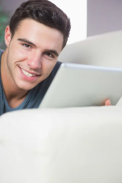 Vrolijke aantrekkelijke man liggend op de Bank met behulp van Tablet PC — Stockfoto