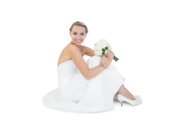 Pretty blonde bride sitting on floor holding a bouquet — Stock Photo, Image