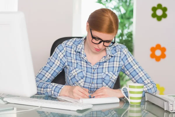 Ruiva escrevendo no bloco de notas em sua mesa — Fotografia de Stock