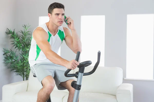 Serious handsome man training on exercise bike phoning — Stock Photo, Image