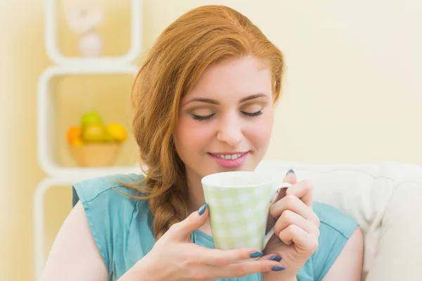 Happy redhead sitting on the couch smelling coffee — Stock Photo, Image