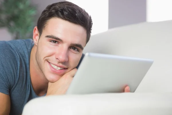 Cheerful handsome man lying on couch using tablet — Stock Photo, Image
