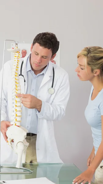 Médico serio mostrando a un paciente algo en el modelo de esqueleto — Foto de Stock