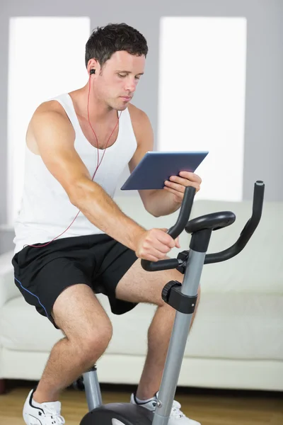 Hombre deportivo guapo haciendo ejercicio en bicicleta y utilizando la tableta — Foto de Stock