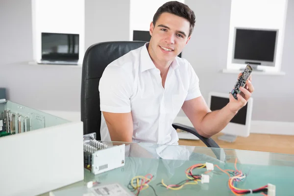 Attractive cheerful computer engineer sitting at desk holding hardware — Stock Photo, Image