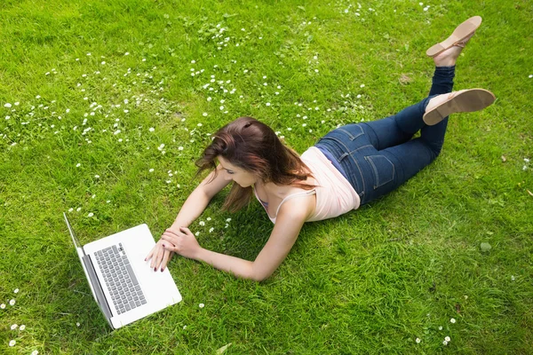 Hübsche junge Frau, die mit ihrem Laptop auf dem Rasen liegt — Stockfoto