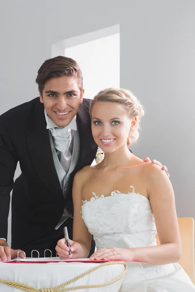 Casal jovem sentado à mesa assinando o registro de casamento — Fotografia de Stock