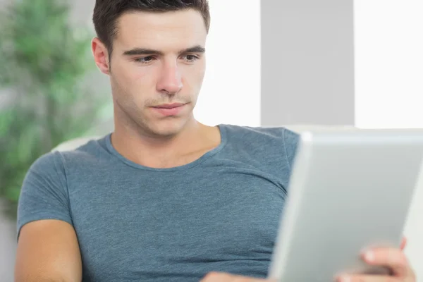 Ernster schöner Mann entspannt sich auf Couch mit Tablette — Stockfoto