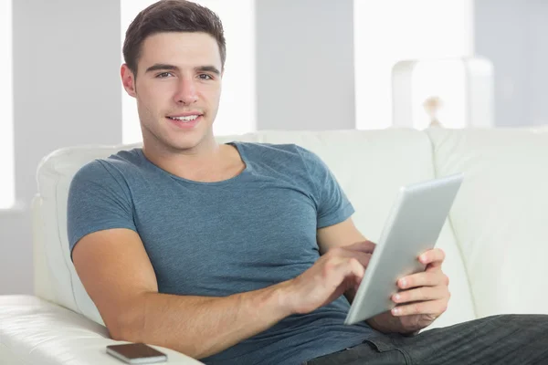 Gülümseyen yakışıklı adam tablet kullanarak kanepede rahatlatıcı — Stok fotoğraf