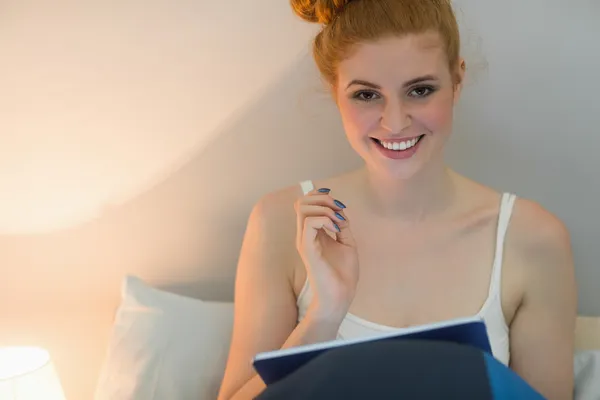 Happy redhead using digital tablet sitting on her bed — Stock Photo, Image