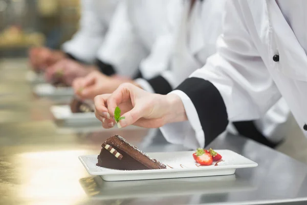 Equipo de chefs en una fila adornando platos de postre — Foto de Stock