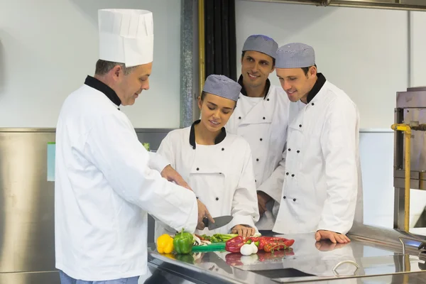 Smiling head chef teaching how to slice vegetables — Stock Photo, Image