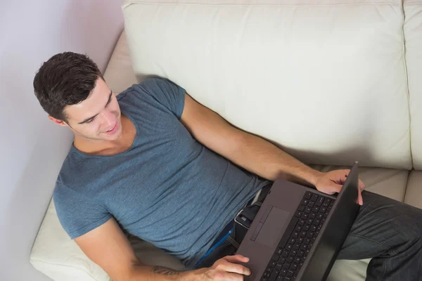 Ansicht des attraktiven Mannes, der es sich mit Laptop auf der Couch bequem macht — Stockfoto