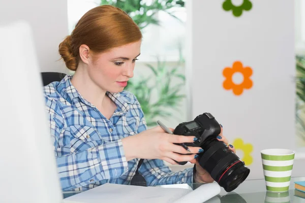 Fokussierte Fotografin sitzt an ihrem Schreibtisch und blickt in ihre Kamera — Stockfoto