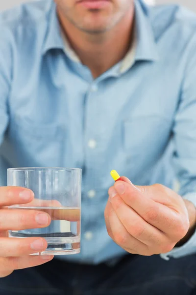 Close up of casual man holding a pill and glass of water — Stock Photo, Image