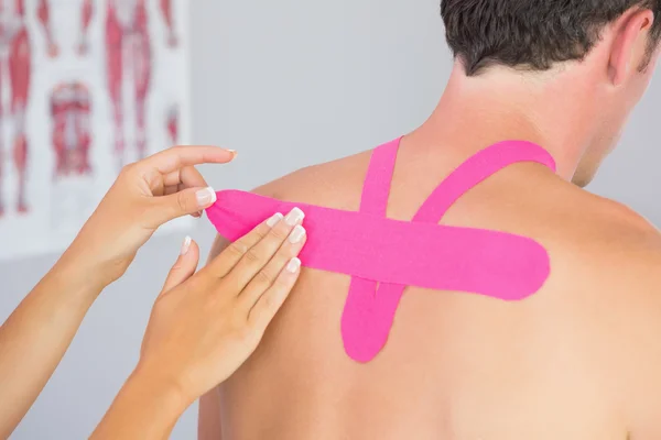 Physiotherapist putting on pink kinesio tape on male patients back — Stock Photo, Image