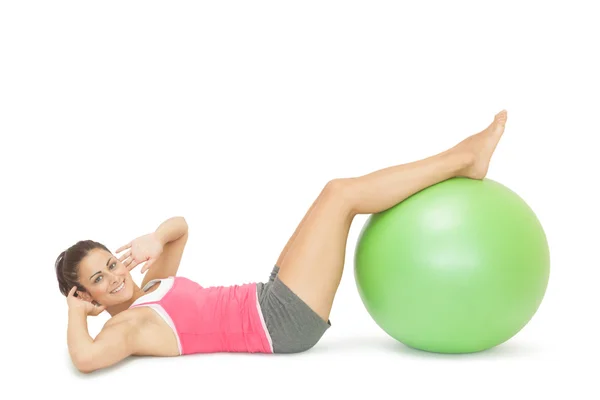 Sorrindo esportivo morena fazendo sit ups com bola de exercício — Fotografia de Stock