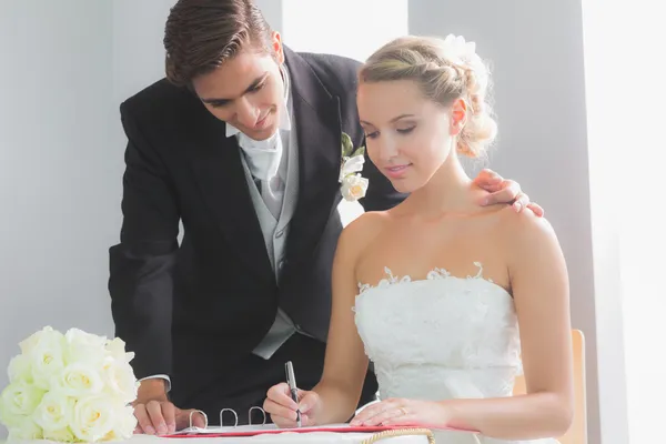 Jonge blonde bruid zitten aan tafel ondertekening bruiloft register — Stockfoto