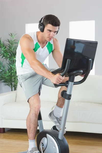 Entschlossener schöner Mann trainiert mit Laptop auf dem Heimtrainer — Stockfoto