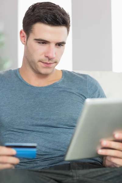 Conteúdo homem bonito relaxando no sofá usando tablet shopping online — Fotografia de Stock