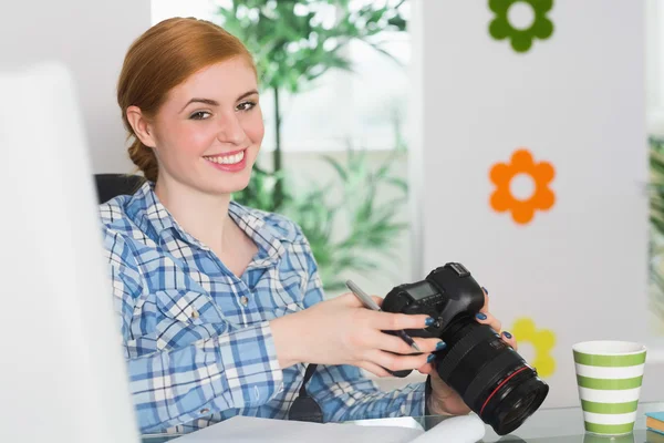 Glückliche Fotografin sitzt an ihrem Schreibtisch und hält ihre Kamera — Stockfoto