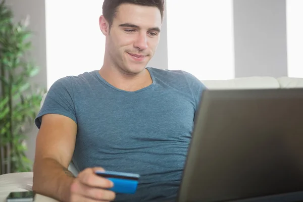 Счастливый красавец отдыхает на диване, делая покупки на ноутбуке в Интернете — стоковое фото