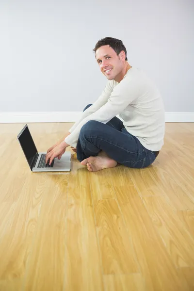 Příležitostné usmívající se muž sedící na podlaze pomocí přenosného počítače — Stock fotografie