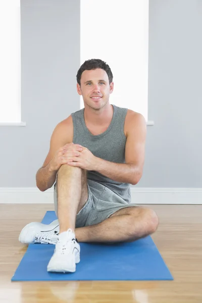 Cheerful sporty man sitting on blue mat Stock Image