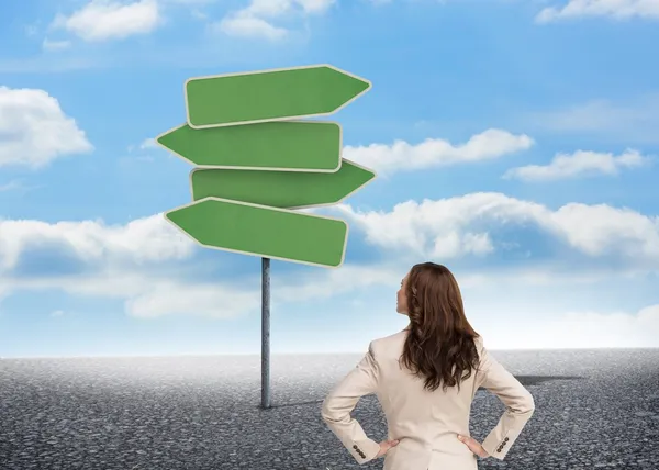 Businesswoman standing back to camera looking at road signs — Stock Photo, Image