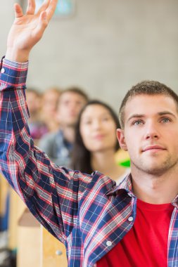 Close-up of a male student raising hand by others in classroom clipart