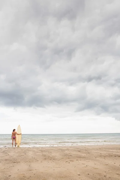 Ruhige Frau im Bikini mit Surfbrett am Strand — Stockfoto