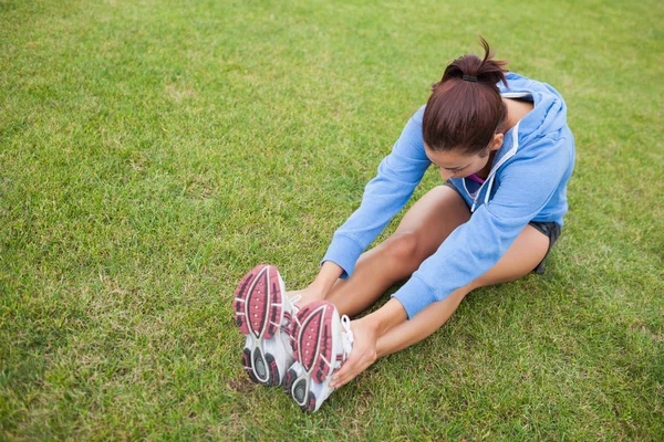 Спортивна жінка розтягує ноги, сидячи на траві — стокове фото