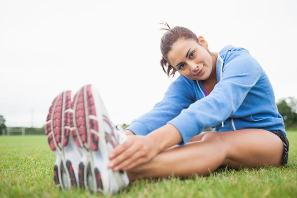 Ziemlich sportliche Frau streckt ihre Beine, während sie auf der Gra sitzt — Stockfoto