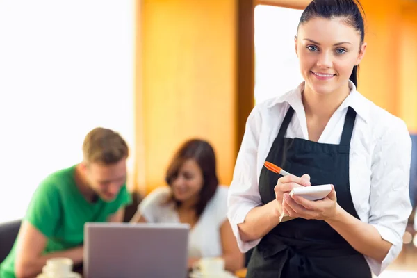 Serveerster schrijven een order met studenten met behulp van laptop op koffie — Stockfoto