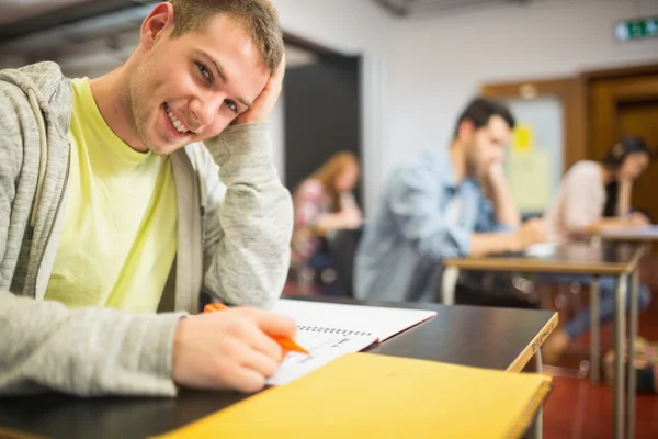 Lachende mannelijke student met anderen schrijven nota's in de klas — Stockfoto