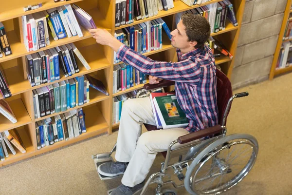 Adam tekerlekli sandalyeye mahkum kütüphanede kitap seçme — Stok fotoğraf