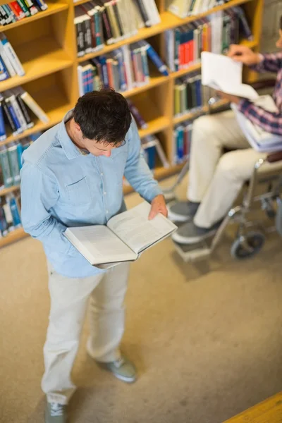 Homem e aluno deficiente em cadeira de rodas lendo livros na biblioteca — Fotografia de Stock
