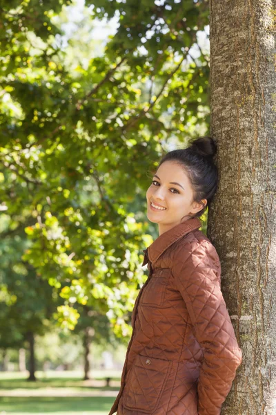 Side view of attractive brunette woman leaning against a tree — Stock Photo, Image