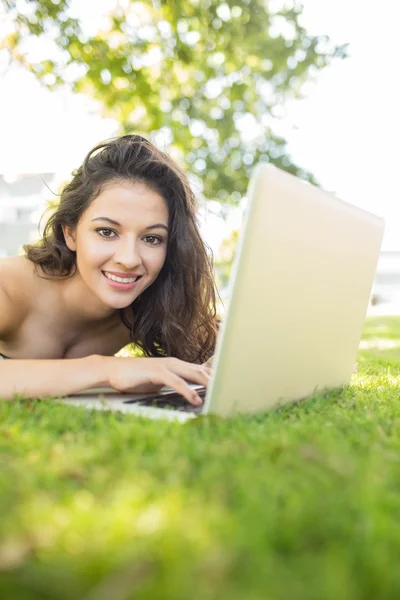 Elegante bruna allegra sdraiata sull'erba usando il suo computer portatile — Foto Stock