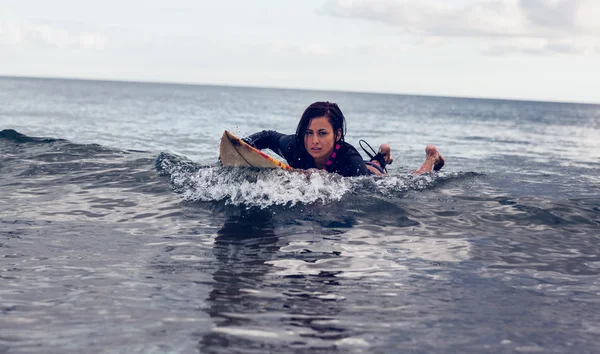 Mujer joven nadando sobre tabla de surf en el agua — Foto de Stock