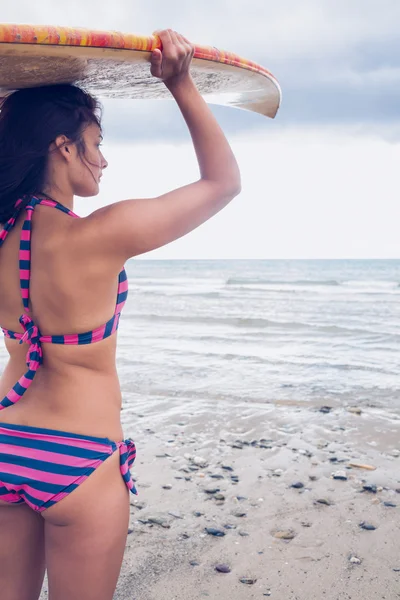 Bikini woman carrying surfboard on head at beach — Stock Photo, Image