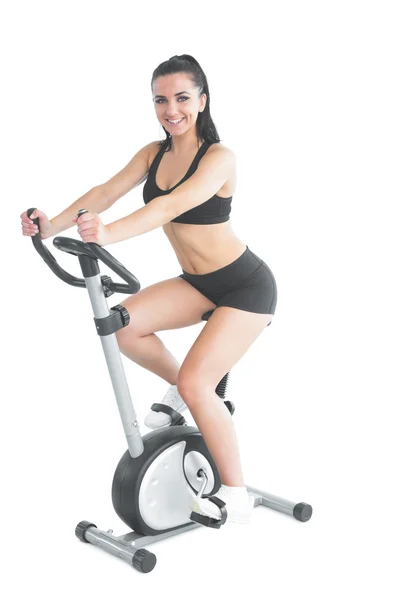 Cheerful ponytailed sporty woman training on an exercise bike — Stock Photo, Image