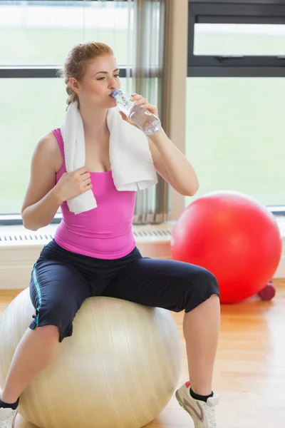 Fitte Frau sitzt auf Gymnastikball und trinkt Wasser — Stockfoto